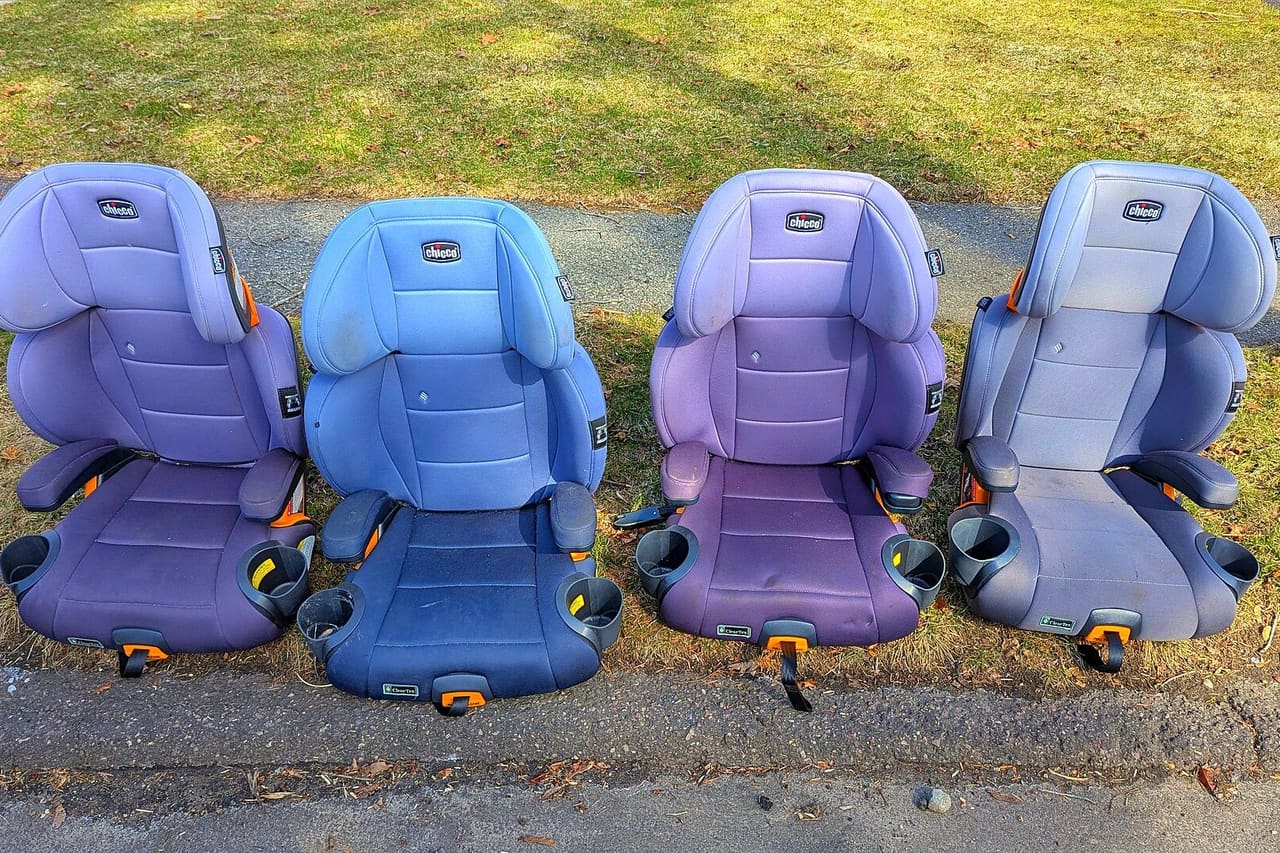 Four high-back booster seats for children lined up on grass